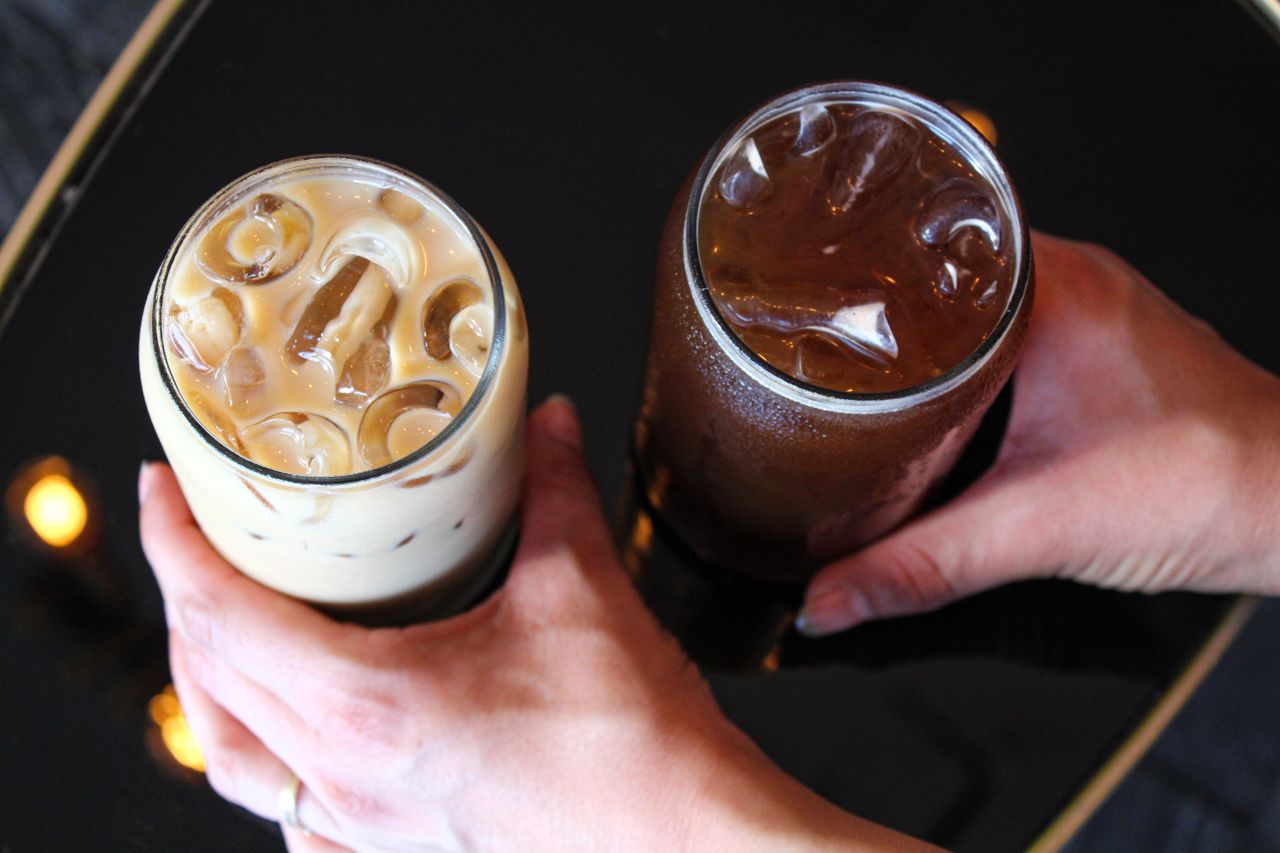Top view of two iced beverages being held over a reflective black surface - perfect for a refreshing break.