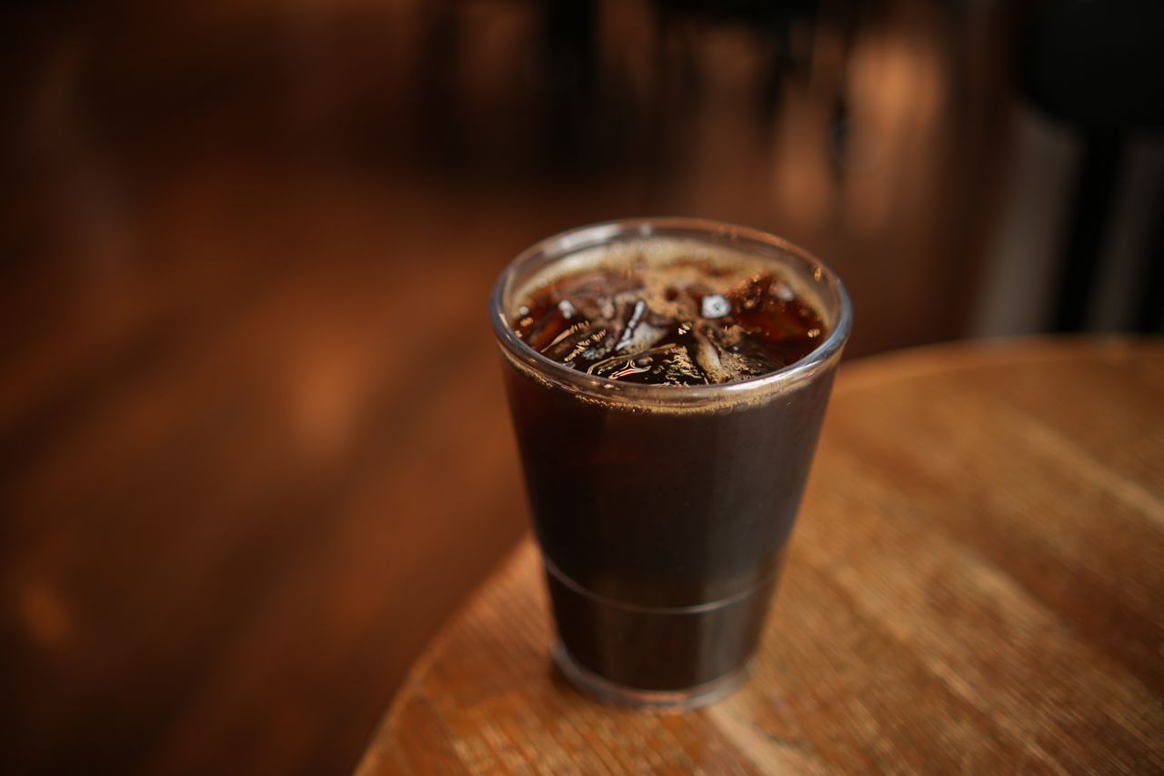 Close-up of a cold brew coffee with ice cubes in a plastic cup on a wooden table indoors.